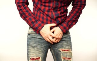 man in jeans and red flannel holds his groin