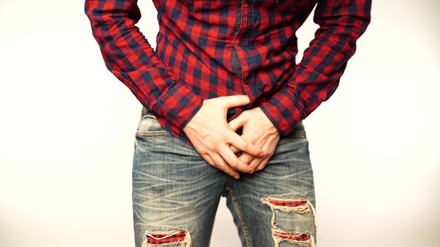man in jeans and red flannel holds his groin